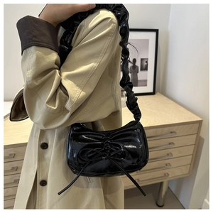 Detail of black glossy shoulder bag featuring chic bow pleats and ruffled strap design
