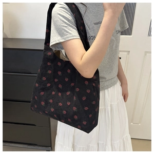 Detail of strawberry print on black corduroy tote bag worn by a model in a home setting