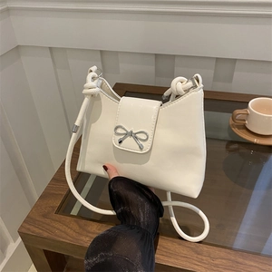 Minimalist white leather underarm bag with a silver metal bow accent and knotted strap