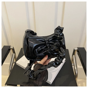 Close-up of black patent leather hobo bag with bow detail and pleated shoulder strap