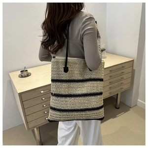 Detailed view of a woven straw tote bag with black stripes and slender shoulder straps