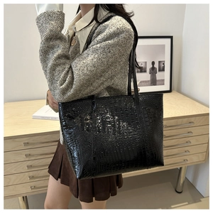 Close-up of black crocodile embossed tote bag with glossy finish and dual shoulder straps