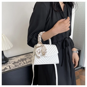 Close-up of a white quilted crossbody bag with a decorative silk scarf wrapped handle