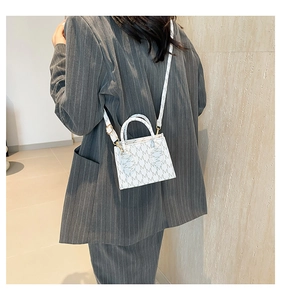 Detail of white box bag with grey 'M' monogram pattern showing handle and crossbody strap