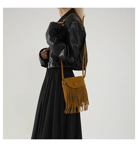 Detail view of ginger yellow crossbody bag with long fringe tassels and a round buckle flap