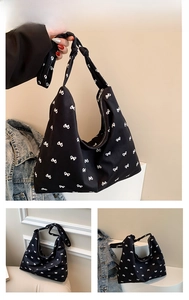 Detail of black canvas tote bag featuring white bow print and knotted shoulder strap