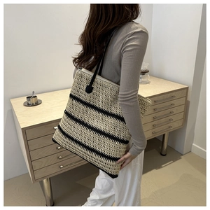 Close-up of a striped woven tote bag with slim black straps and zipper on a female model