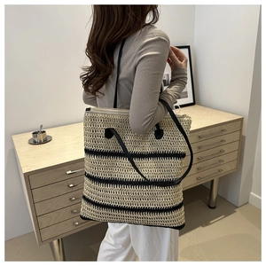 Detailed side view of the large striped straw tote bag worn by a model in a minimal room
