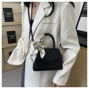 Detail of black quilted crossbody bag with silk scarf handle on a white blazer