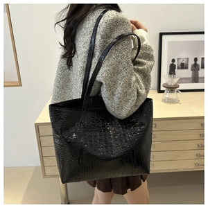 Detail of high-gloss black crocodile embossed tote bag worn over the shoulder
