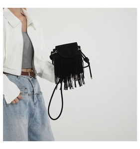 Detail of a black tassel crossbody bag showing suede texture and bohemian fringe style