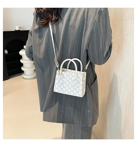 Detail view of mini white crossbody bag with M-pattern print and gold hardware worn by model