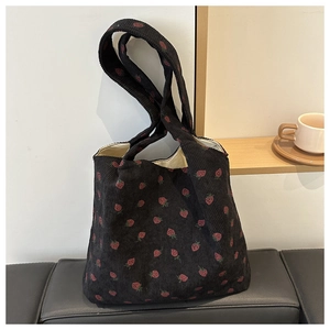Detail view of a black corduroy tote bag featuring a cute strawberry print on a leather bench