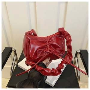 Detail of red bow handbag with ruched handle and glossy leather finish texture