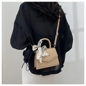 Detail of a beige quilted crossbody bag featuring a silk scarf wrapped handle decoration