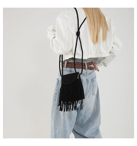 Detail of a black crossbody bag with long fringes shown on model with white jacket