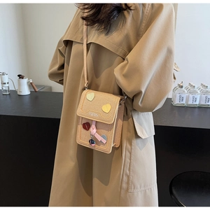Close-up of woven crossbody bag with heart patches and ribbon on khaki coat