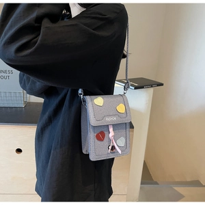 Detail of gray crossbody phone bag featuring heart patches and fashion lettering