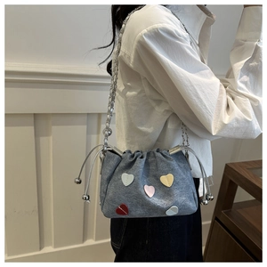 Detail of blue denim bucket bag with colorful heart patches and silver chain strap