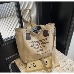 Detail of beige canvas tote bag showing side pocket, leather handles and crossbody strap