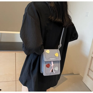 Detail of grey crossbody bag featuring colorful heart patches and fashion print on the flap