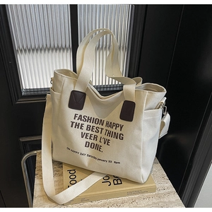 Detail of cream canvas tote bag with brown leather accents and artistic lettering print