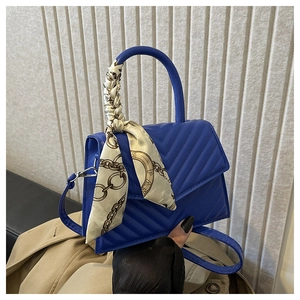 Detail of royal blue quilted handbag with V-shaped stitching and Paris print silk scarf