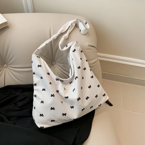 Chic white canvas hobo bag with black bow patterns on an elegant cream sofa