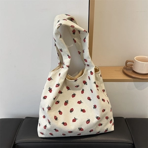 Off-white corduroy tote bag with strawberry print shown on a leather chair