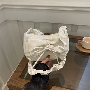 Minimalist white bow shoulder bag with ruffled handle on a dark wooden table