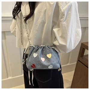 Dettaglio borsa a secchiello in denim blu con toppe a cuore colorate e coulisse a catena