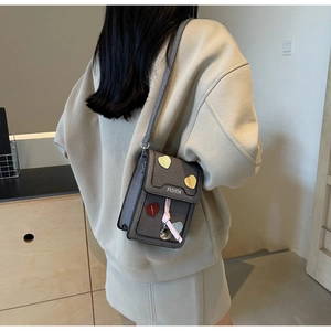 Detail of grey crossbody bag with colorful heart patches and pink tassel pendant
