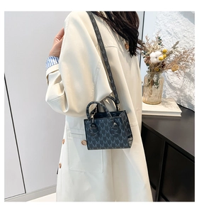 Detail of grey crossbody bag with M-pattern print and golden hardware on a model