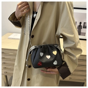 Dettaglio di borsa a secchiello nera con cuori colorati e tracolla a catena su un trench