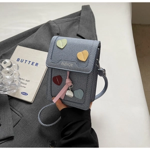 Detail of blue denim crossbody bag with colorful heart patches and fashion embroidery