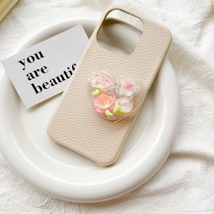 Close-up of beige leather phone case with 3D pink and white floral charms on a ceramic plate