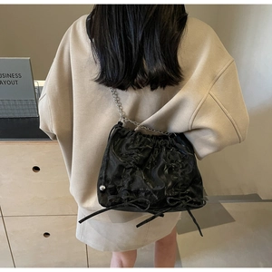 Détail du sac seau noir plissé avec nœuds décoratifs et fine bandoulière en chaîne