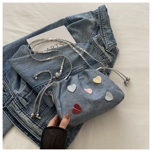 Dettaglio borsa a secchiello in denim blu con patch a cuore colorate e tracolla a catena