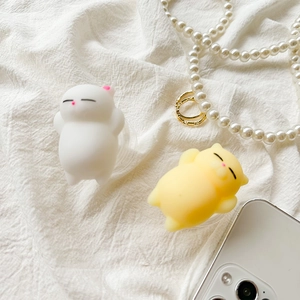 Close-up of cute cat-shaped squeeze silicone phone grips on white fabric with accessories
