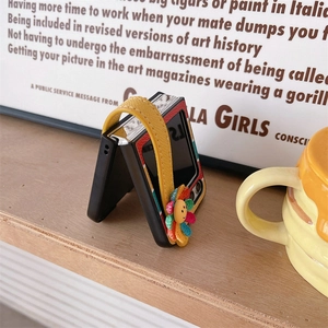 Detail of Galaxy Z Flip case featuring a yellow leather wrist strap and a colorful sun flower charm