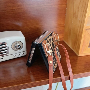 Detail of leopard print foldable case with leather crossbody strap and gold metal buckles