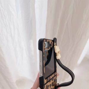 Detail view of leopard print folding phone case with wrist strap and white flower charm