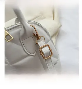 Close-up of white quilted crossbody shell bag showing gold hardware and precise stitching