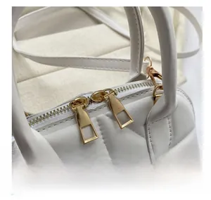 Detail of white quilted shell bag showing smooth gold zippers and metal hardware