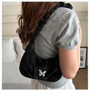 Detail of black crescent shoulder bag featuring silver butterfly buckle and pleated strap