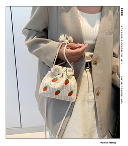 Detail of mini straw bucket bag featuring red strawberry embroidery and drawstring closure