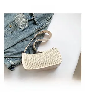 Close-up of cream woven underarm bag with silver stud strap on minimalist desk