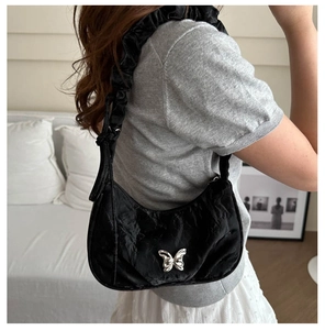 Detail of black pleated underarm bag with silver butterfly charm shown on shoulder