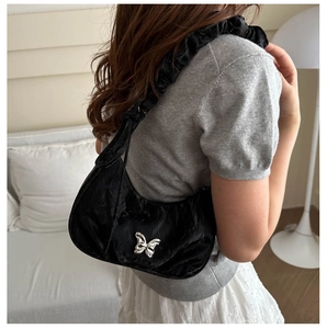 Detail of black pleated crescent shoulder bag with silver butterfly and ruffled strap