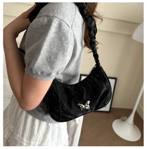 Detail of black crescent shoulder bag with silver butterfly charm and ruched strap